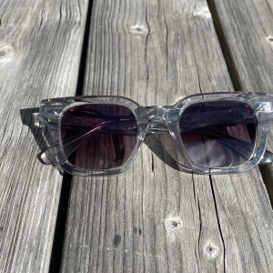 Chimi 04 - Snygga solglasögon från Chimi med transparent, fyrkantig båge och mörka linser. Riktigt clean och modern look, perfekt för dig som vill sticka ut med stilren design. Bågarna är i plast och rostfritt stål och designade i Stockholm.