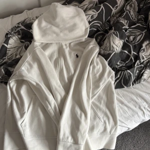 Vit zip hoodie från Polo Ralph Lauren - Vit hoodie från Polo Ralph Lauren med dragkedja och klassisk broderad logga på bröstet. Tröjan har huva med snörning, fickor framtill och är tillverkad i mjuk bomull. Perfekt för en chill och stilren look. Det går själv klart o diskutera priset 