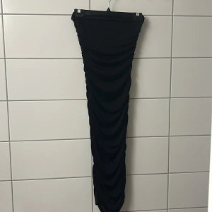 Svart långkjol med rynkade detaljer.  - Säljer en svart långkjol med tight passform och snygga rynkade detaljer längs hela kjolen. Kjolen har en elastisk midja och är gjord i ett stretchigt material som sitter snyggt på kroppen. Perfekt för dig som gillar en stilren och trendig look.
