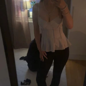 Ljus rosa korsett-topp med volang - Supersnygg ljus rosa korsett-topp med markerade sömmar och volang nertill. Axelbandslös design som ger en feminin siluett och passar perfekt till både jeans och kjol. Materialet känns mjukt och följsamt mot huden.