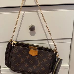 Louis Vuitton Monogram axelväska - Säljer en brun axelväska från Louis Vuitton med klassiskt monogrammönster och guldiga detaljer. Väskan har två fack, rund myntplånbok och både kedje- och bred blå axelrem. Perfekt för dig som vill ha en ikonisk och trendig accessoar.den är i en väldigt bra form/kvalitet priset kan diskuteras 🤍