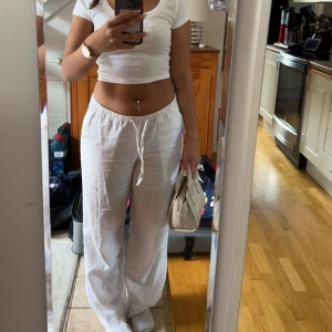 Vita linnebyxor med snörning - Säljer ett par vita, luftiga linnebyxor med snörning i midjan. Byxorna har en avslappnad passform och raka ben, perfekta för varma dagar. Superbekväma och lätta att styla med crop tops eller linnen.