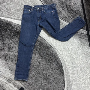Levi's blå jeans skinny fit - Säljer ett par klassiska blå Levi's jeans i skinny fit med fem fickor och snygga kontrastsömmar. Jeansen har det ikoniska läderpatchen bak i midjan och röd Levi's-tag på bakfickan. Perfekta för dig som gillar en smalare passform och tidlös denimstil.