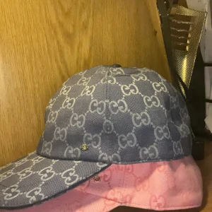 Gucci keps dubai kombination rosa och blå - Två snygga Gucci kepsar i klassisk modell, en i blått och en i rosa. Båda har det ikoniska GG-mönstret över hela kepsen och är tillverkade i slitstark bomullscanvas. Perfekt accessoar för att lyfta din outfit med lyxig streetstyle-vibe.
