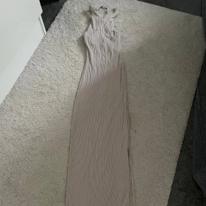 Beige ribbad långklänning från BERSHKA  - Supersnygg beige långklänning med ribbad struktur och ärmlös design från BERSHKA. Klänningen har en smickrande, figurnära passform och är perfekt för dig som gillar stilrena och enkla plagg. Passar lika bra till sneakers som till klackar.