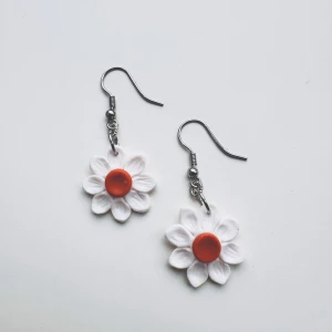 Blommiga örhängen - Superfina örhängen i form av vita blommor med en orange mitt. Hängande modell med metallkrok, perfekt för dig som vill ha något unikt. Blommorna är detaljerade och ger en söt och somrig vibe. Metallen är av Nickelfritt kirurgiskt stål.