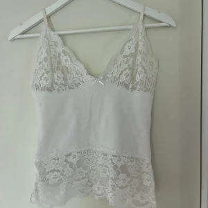 Spetsigt vitt linne - Snyggt linne med spetsdetaljer. Märke okänt, köpt på second hand men har själv aldrig använt den. En söt rosett i mitten.