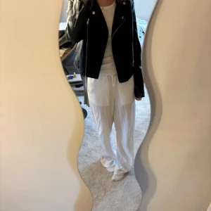 Svart skinnjacka med dragkedjor - Säljer en svart skinnjacka med coola silvriga dragkedjor och klassisk bikerstil. Jackan har flera fickor med dragkedja och snygga detaljer vid axlar och ärmslut. Perfekt för dig som vill ha en edgy look till vardags. Passformen är normal och jackan är långärmad.