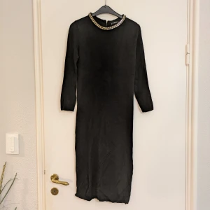 Finstickad svart klänning från Zara Knit - Finstickad svart klänning från Zara Knit med snygg guldfärgad detalj runt halsen. Klänningen har dragkedja bak för enkel påklädning. Är tight i passformen och väldigt skön mot huden. Perfekt för dig som vill ha en stilren och elegant look.