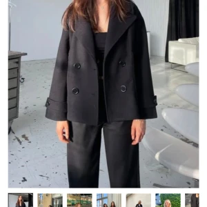 Svart skepparkavaj med knappar - Stilren svart skepparkavaj med dubbelknäppning och bred krage. Jackan har en loose passform och långa ärmar med dekorativa knappar vid ärmslut. Perfekt för dig som gillar en klassisk men cool look.