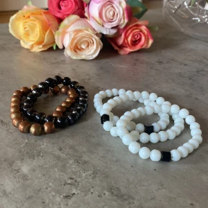 Set med pärlarmband i olika färger - Fyra elastiska armband med runda pärlor. Två armband är i svart och bronsfärg, de andra två är vita med svarta detaljer. Perfekta att mixa och matcha för en cool och personlig stil. Passar både till jeans och klänning.