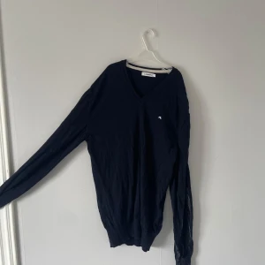 Mörkblå stickad tröja från J.Lindeberg - Snygg mörkblå v-ringad tröja från J.Lindeberg med liten broderad logga på bröstet