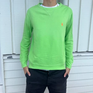 Polo Ralph Lauren tröja  - Fräsch grön crewneck från Polo Ralph Lauren med orange broderad logga på bröstet. Tröjan har rund halsringning och är tillverkad i en mjuk mix av bomull, polyester och modal. Perfekt för dig som gillar färg och klassisk stil.