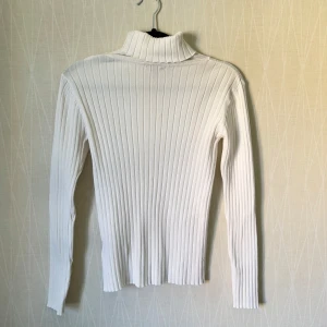 Vit ribbad polotröja från Lindex - Vit ribbad polotröja från Lindex i storlek S. Tröjan har lång ärm, hög polokrage och är figurnära i modellen. Perfekt att styla med jeans eller kjol för en clean och snygg look.