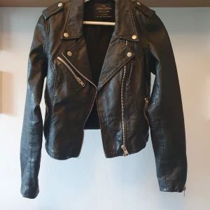Svart (äkta) skinnjacka från Zara i storlek small - Svart skinnjacka i äkta (lamm)skinn med dragkedja och tryckknappar från Zara. Jackan har en klassisk biker-modell med dragkedjor på framsidan och ärmarna. 🖤 Bomullsinnertyg med polyestertyg i ärmarna för att den ska vara lätt att få på. Mindre slitningar finns men de syns endast på nära håll. Ett liiitet hål uppe på ena axeln (döljs om man har medellångt hår) som säkert går att fixa om man lämnar in den hos någon. Tror den köptes för ca 2000kr. Yttermaterial 100% läder (se tvättlapp på bild) 