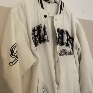 Vit jacka med tryck - Snygg vit bomberjacka med svarta detaljer och stora tryck på bröstet och ärmen. Jackan har klassisk krage med svarta ränder. Perfekt för dig som gillar sportig streetstyle.     Storlek S och köpt på H&M! Skriv om du har frågor eller vill ha fler bilder!😍