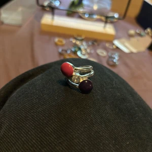 Cool silverring med färgade stenar - Unik silverfärgad ring med två stora stenar i lila och rosa samt en klar sten i mitten. Ringen har en modern, chunky design med öppet band som ger en edgy vibe. Perfekt för dig som vill sticka ut med accessoarer som syns.