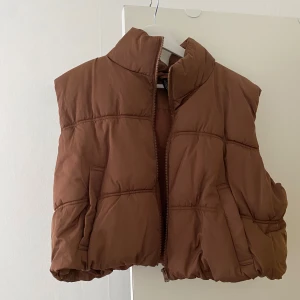 Brun dunväst från Divided, XL - Säljer en brun, quiltad dunväst från Divided i storlek XL. Västen har hög krage, dragkedja framtill och två fickor på sidorna. Cropped fit, nyttskick prislapp hänger kvar.