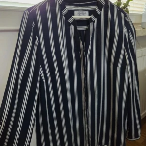 Randig overshirt från Bariloche - Snygg marinblåvit randig overshirt från Bariloche, tillverkad i Spanien. Lätt och luftig med lång ärm och klassisk krage. Perfekt för dig som gillar stilrena och trendiga plagg med lite extra edge.