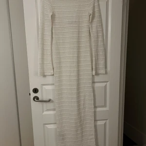 Vit lång strandklänning - Superfin långklänning i vitt med stickad struktur och horisontella ränder. Klänningen har lång ärm och en djup, rundad rygg. Perfekt för dig som gillar en mysig men ändå stilren look.