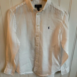 Vit linneskjorta från Polo Ralph Lauren - Klassisk vit skjorta från Polo Ralph Lauren i luftig linne. Broderad marinblå logga på bröstet ger en clean och stilren look | Skick: 9/10 som ny | Ny pris: 1200kr - Mitt pris: 399kr | Storlek: L (Barn) - Passar XS - S beroende på hur du vill att skjortan ska sitta | var inte rädd att höra av dig vid funderingar 📩