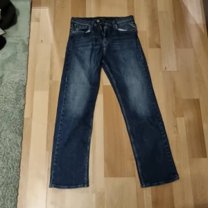 Blå raka jeans från Replay - Snygga blå jeans från Replay med klassisk femficksdesign och raka ben. Jeansen har en mörk tvätt med lätt slitning och tydliga sömmar. Märkespatch bak i midjan och diskret logga på bakfickan. Perfekta för en avslappnad och stilren look. Inga detekter, säljer pga passar ej längre