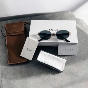 Celine ovala solglasögon i silver - Snygga ovala solglasögon från Celine med tunna silverfärgade metallbågar och svarta glas. Klassisk och stilren design med svarta skalmar och exklusiva detaljer. Kommer med originalfodral i brunt och putsduk.