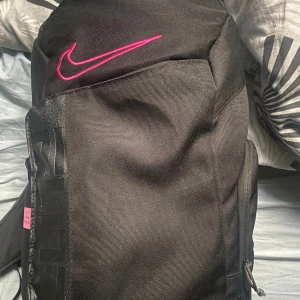 Nike Elite svart ryggsäck med rosa detaljer - PRIS KAN DISKUTERAS! Säljer en Nike Elite ryggsäck i svart med snygga rosa detaljer och logga. Väskan har vadderade axelremmar med transparenta partier, flera fack med dragkedja och meshficka på sidan. Perfekt för träning eller skola, rymmer mycket och är riktigt stilren.