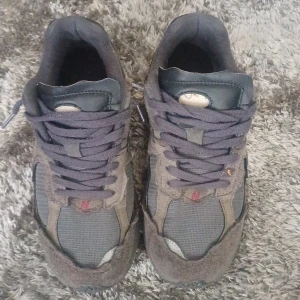 New Balance 2002R sneakers grå/brun - Snygga New Balance 2002R sneakers i en mörkgrå och brun färgskala. Ovandel i mesh och mocka med klassisk N-logga på sidan. Skorna har snörning och en chunky sula som ger skön komfort. Perfekta för dig som gillar streetwear och vill ha en stilren look.