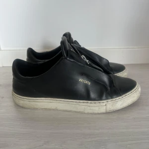 Svarta sneakers från Axel Arigato - Stilrena svarta sneakers från Axel Arigato i skinn med vit sula och cool dragkedjedetalj på ovansidan. 