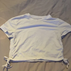 Vit croppad topp med knyt i sidan - Säljer en vit croppad topp i bomull med korta ärmar och snygga knytband i sidorna. Toppen har en enkel och clean look, perfekt att styla med jeans eller kjol. Sidorna har rynkade detaljer som ger en cool touch.