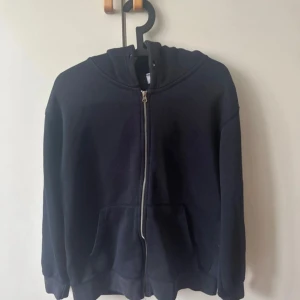 Marinblå hoodie med dragkedja från Zara - En svart hoodie från Zara i storlek L med dragkedja framtill och huva. Tröjan har två stora fickor på magen och är tillverkad i mjuk bomull. Passformen är lite loose och ärmarna är långa, perfekt för chill dagar. Den är storlek L på Zaras mansavdelning (om jag ej har fel)