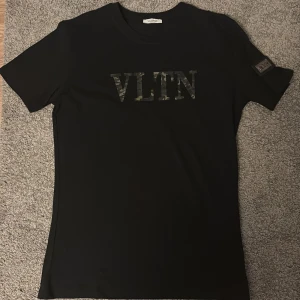 Svart Valentino VLTN t-shirt med camo - Svart t-shirt från Valentino med VLTN-logga i camouflagemönster på bröstet och patch med VLTN på ärmen. Klassisk passform, rund hals och korta ärmar. Perfekt för dig som gillar stilrena plagg med en twist. Vill få sålt den snabbt, priset e ej hugget i sten så kom med förslag vid minsta fråga.