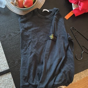 Mörkblå långärmad tröja från Stone Island - Säljer en mörkblå långärmad tröja från Stone Island. Tröjan har en rund halsringning och det ikoniska märket på ärmen. Perfekt för en stilren och avslappnad look.