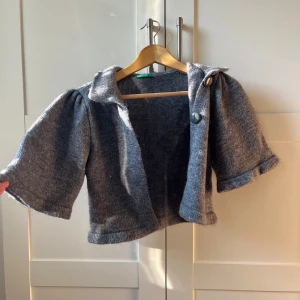 Grå bolero i ull - Säljer en grå stickad cardigan jacka med trekvartsärm och stora knappar. Perfekt för lager-på-lager-stil och ger en mysig känsla. I ull
