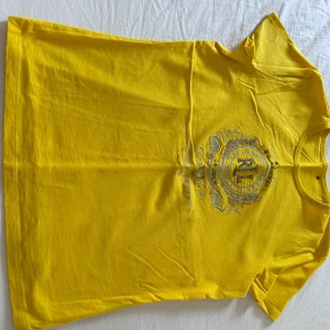 Gul t-shirt från Ralph Lauren - Säljer en snygg gul t-shirt från Ralph Lauren med ett detaljerat silverbroderi på framsidan. Perfekt för att liva upp garderoben med lite färg! Skriv vid intresse!!