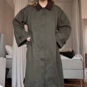 Grön trenchcoat med brun krage - Säljer en oversized grön trenchcoat med brun krage. Jackan har långa ärmar, dold knäppning framtill och justerbara ärmslut❣️ Köptes för 1199kr men säljer för 900kr. Använt ett fåtal gånger 