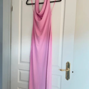 Ljusrosa långklänning med draperad hals - Säljer en ljusrosa långklänning med draperad halsringning. Klänningen har en slits framtill och är tillverkad i ett mjukt, slätt material som faller snyggt. Perfekt för sommarens tillfällen!