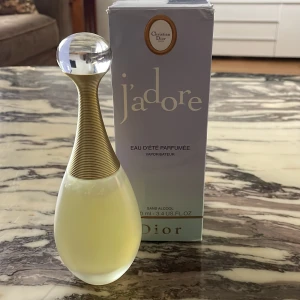 J'adore Eau d'Été Parfumée från Dior - Lyxig parfym från Dior, J'adore Eau d'Été Parfumée. Flaskan är elegant med droppformad design, frostat glas och guldfärgad hals. Kommer med originalkartong i ljuslila med gulddetaljer. Innehåller 100 ml. Aldrig använd och perfekt för sommarn