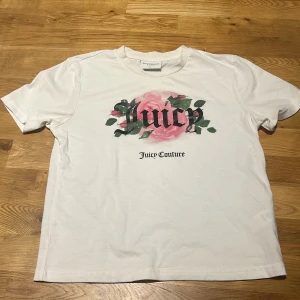 Vit t-shirt med ros-tryck från Juicy Couture - Vit t-shirt från Juicy Couture med tryck av en rosa ros och texten 'Juicy' på bröstet. Klassisk passform och rund halsringning. Perfekt för dig som gillar stilrena plagg med en touch av blommigt. Storlek large men passar perfekt till någon som har small också, knappt använt.