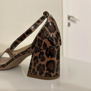 Leopardmönstrade sandaler med blockklack - Säljer ett par sandaler med leopardmönster och bred blockklack. Skorna har öppen tå och justerbar rem runt vristen. Perfekta för dig som vill sticka ut med ett djurmönster och samtidigt ha bekväma klackar.