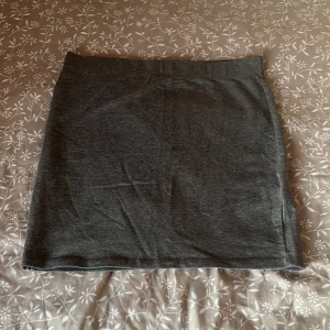 Mörkgrå enkel kjol - Säljer en mörkgrå, rak och enkel kjol i mjukt material. Kjolen har en klassisk, stilren design utan synliga detaljer och passar perfekt till många olika outfits. Midjelinningen är elastisk för extra komfort.