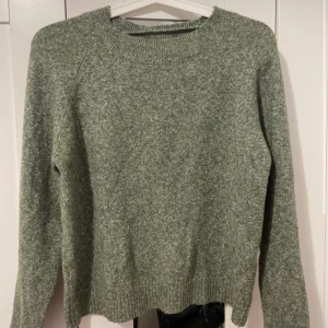 Grön stickad tröja - Mysig grön stickad tröja med rund halsringning och långa ärmar. Tröjan har en enkel och klassisk design med ribbade muddar vid ärmslut och nederkant. Perfekt för kyliga dagar.