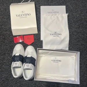 Valentino Garavani skor  - Snygga vita Valentino Garavani sneakers med svarta detaljer och nitar. Skorna har en klassisk rund tå och snörning framtill. Perfekta för att ge en stilren touch till din outfit. Hör av er vid minsta fundering 🍾Priset kan diskuteras 🍾