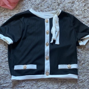 Svart kortärmad topp med knappar -  svart topp med vita detaljer och knappar framtill. Den har en knytning vid halsen och korta ärmar. 💖