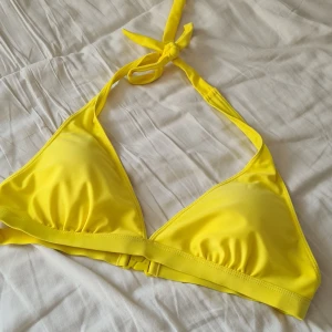 Gul trekantsbikini - Säljer en snygg gul trekantsbikini med knyt i nacken och spänne i ryggen. Bikinin har en klassisk och enkel design, perfekt för stranden eller poolen. Materialet känns mjukt och följsamt, med uttagbara inlägg.💕