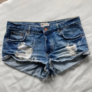 Blå jeansshorts  - Säljer ett par lågmidjade blå jeansshorts med slitningar! Midjemåttet tvärs över är 39cm och grenlängden 21cm💕Pris kan diskuteras!