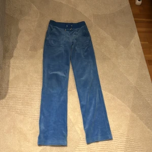 Blå mjukisbyxor från Juicy Couture - Säljer ett par blå mjukisbyxor från Juicy Couture. Byxorna har en loose passform med snörning i midjan och fickor med knappar bak. Perfekta för en avslappnad stil. Säljer för att dom ej kommer till användning längre. 