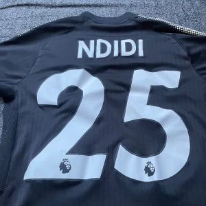 Svart Leicester City fotbollströja från Puma - Säljer en svart Leicester City fotbollströja från Puma med guldiga detaljer. Tröjan har korta ärmar och klubbens emblem på bröstet. Perfekt för fans av Leicester City!