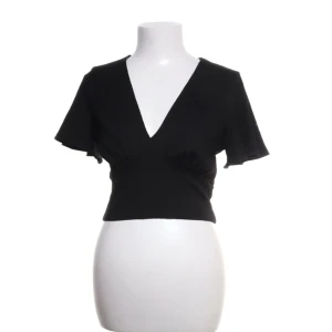 Svart v-ringad topp - Snygg svart topp med v-ringning och korta ärmar. Den har en croppad passform som ger en modern look. Perfekt för att styla med höga jeans eller kjol.